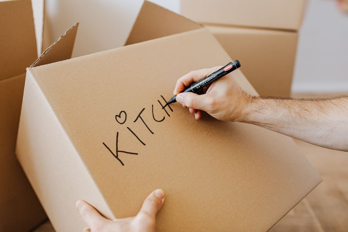A moving box being marked with the destination room in marker pen